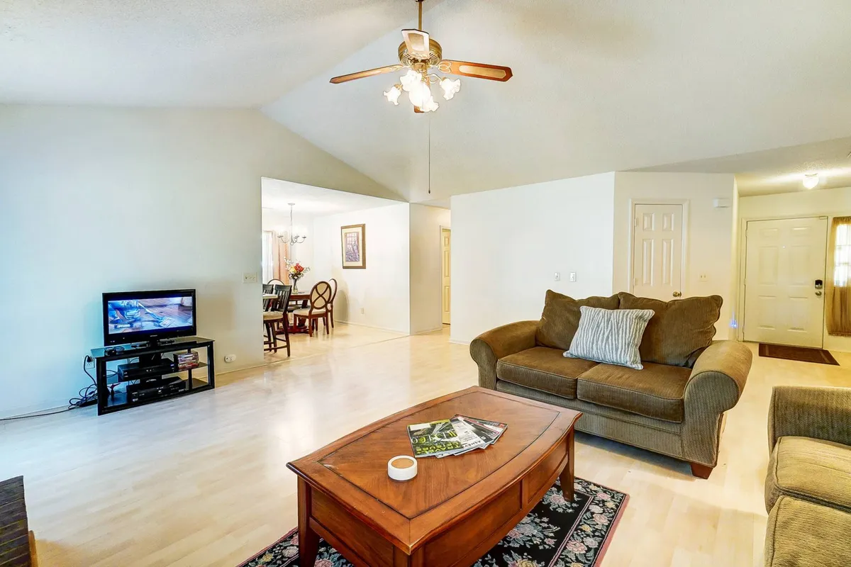 A spacious, comfortable living area with a sofa, coffee table, television, and visible dining area in the background. The arrangement invites both relaxation and social interaction, seamlessly blending lounging and dining spaces.
