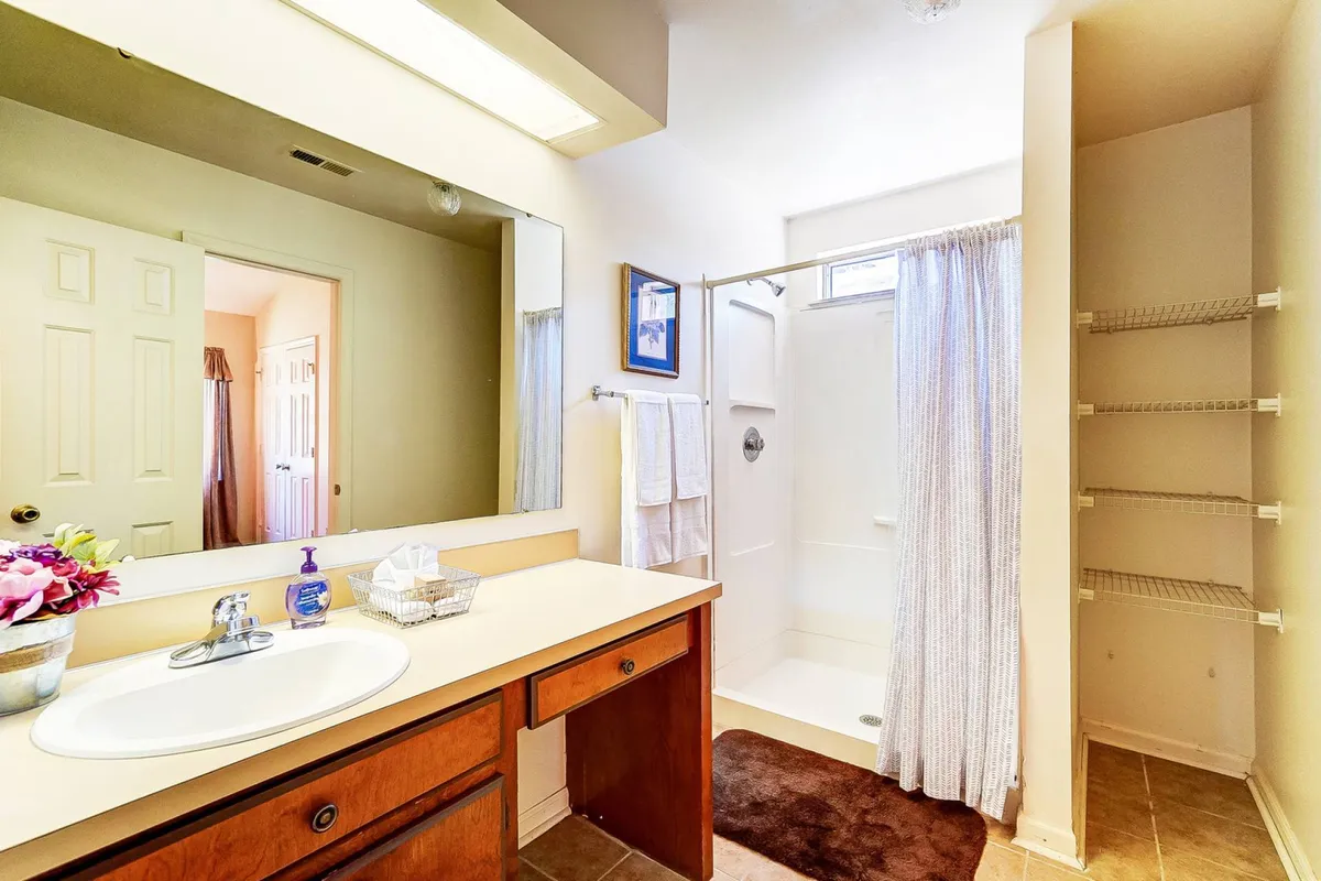 A sparkling clean bathroom featuring a modern vanity with a sink, mirrored cabinet, a walk-in shower area, and shelves stocked with fresh towels and toiletries. The room feels bright and inviting, ideal for personal grooming and relaxation.