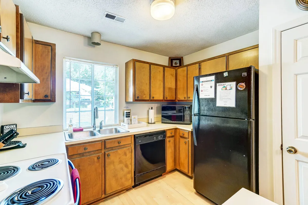 A practical, homey kitchen with a black refrigerator, spacious wooden cabinets, and a sink, ideal for preparing family meals and gathering for brunches or cooking nights.