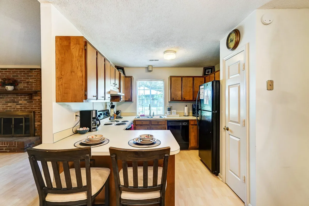 A bright, inviting kitchen with a central island, modern black appliances, wooden cabinets, and a window that lets in natural light. The kitchen is tidy and functional, with comfortable seating at the island, creating a perfect spot to enjoy a morning coffee or catch up on emails.